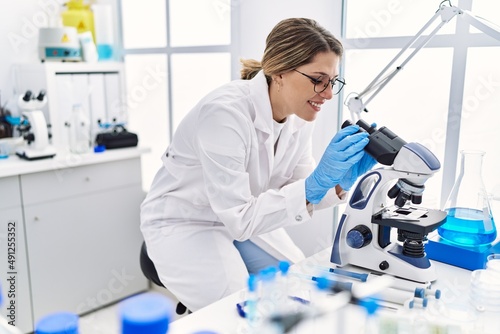 Young hispanic woman wearing scientist uniform using microscope at laboratory