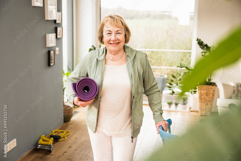 Happy senior woman standing with exercise mat at home Happy senior woman standing with exercise mat at home