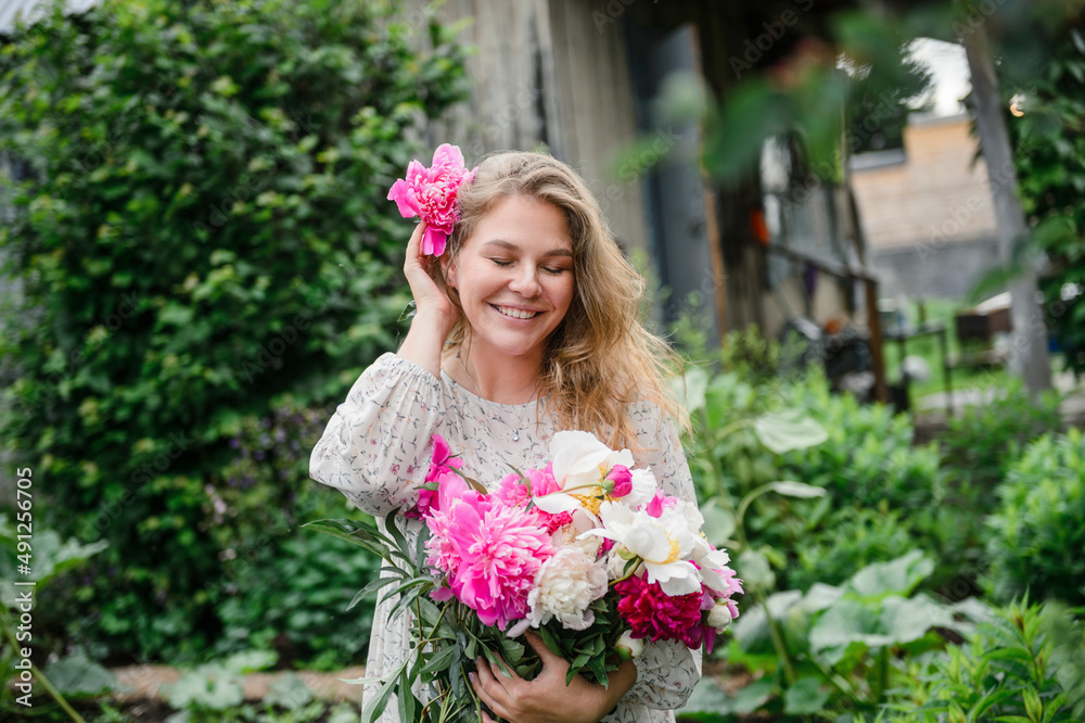 Beautiful smiling blond woman wearing pink flower standing in garden Beautiful smiling blond woman wearing pink flower standing in garden