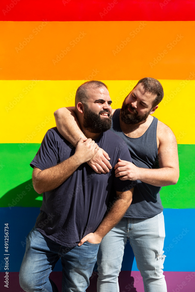 Obraz premium Young gay couple hugging on a background with rainbow colors. LGBT pride concept.