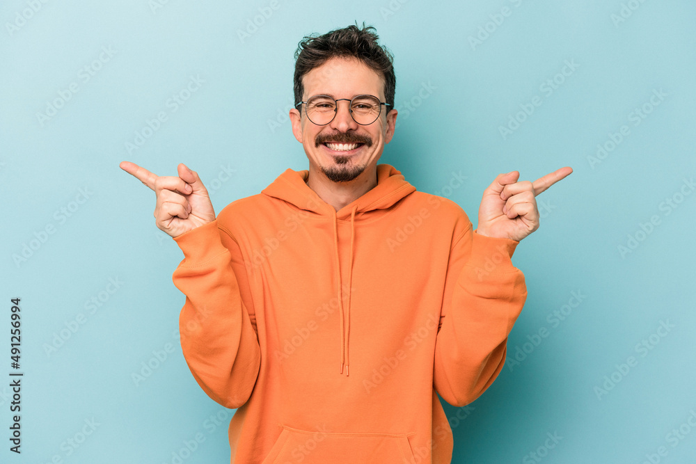 Fototapeta premium Young caucasian man isolated on blue background pointing to different copy spaces, choosing one of them, showing with finger.