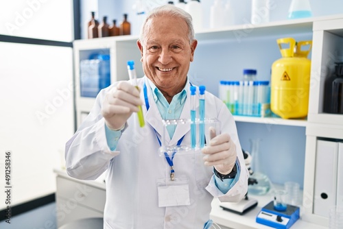Senior man wearing scientist uniform holding test tubes at laboratory