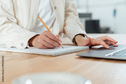 Entrepreneur writing on notepad and using laptop at workshop photo