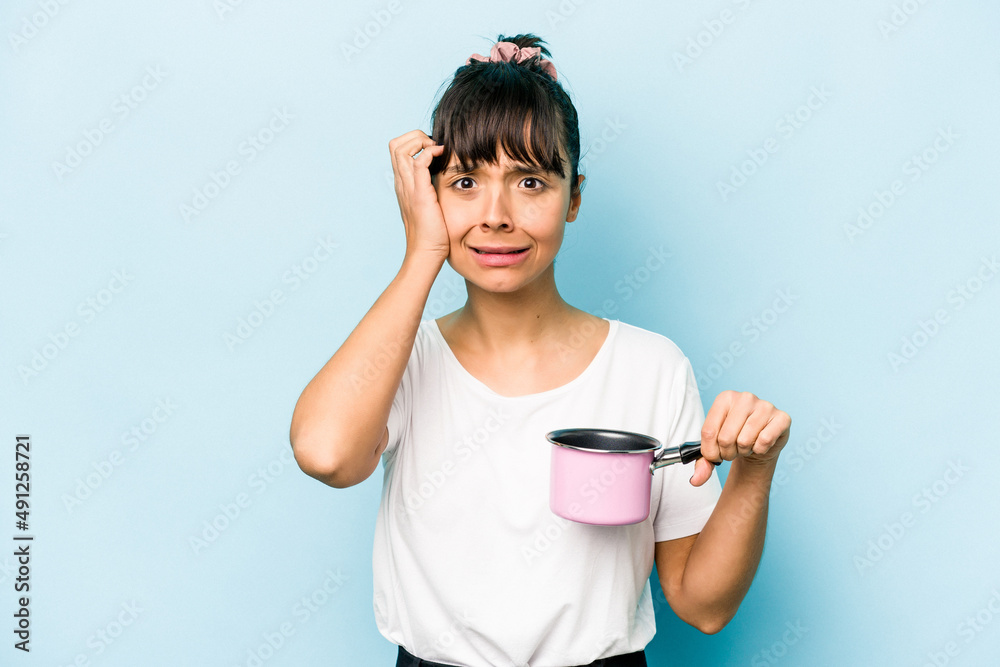 Young hispanic woman holding a saucepan isolated on blue background being shocked, she has remembered important meeting. Young hispanic woman holding a saucepan isolated on blue background being shocked, she has remembered important meeting.