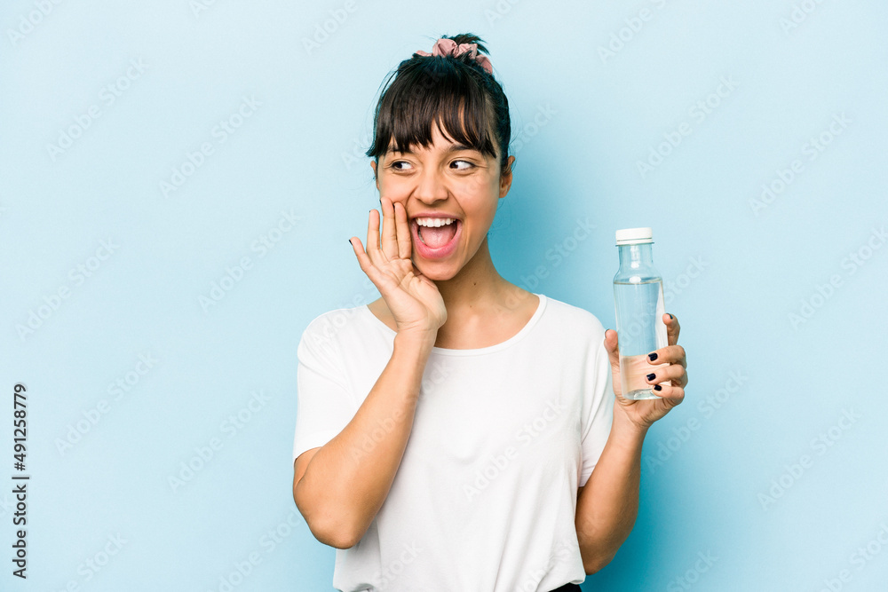 Young hispanic woman holding a bottle of water isolated on blue background shouting and holding palm near opened mouth. Young hispanic woman holding a bottle of water isolated on blue background shouting and holding palm near opened mouth.