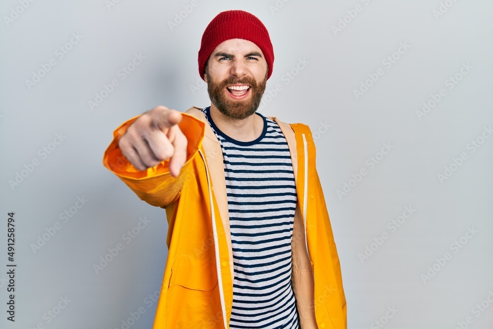 Caucasian man with beard wearing yellow raincoat pointing displeased and frustrated to the camera, angry and furious with you