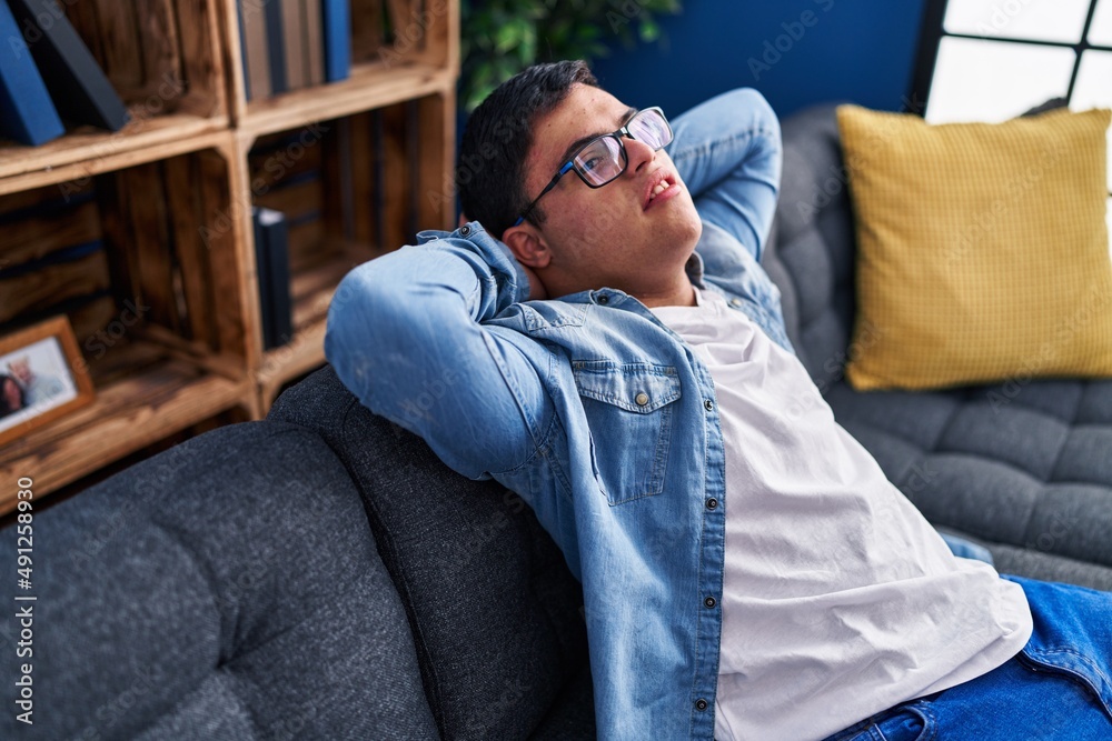 Fototapeta premium Down syndrome man relaxed with hands on head sitting on sofa at home