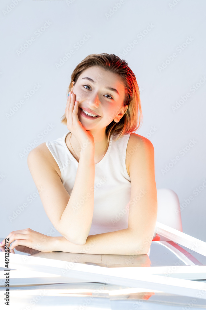 Pretty face. Facial skincare. Rejuvenation treatment. Portrait of happy smiling girl with flawless skin in red neon light isolated on neutral white. Pretty face. Facial skincare. Rejuvenation treatment. Portrait of happy smiling girl with flawless skin in red neon light isolated on neutral white.