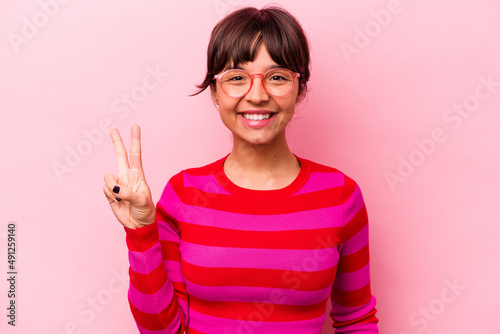 Young hispanic woman isolated on pink background showing victory sign and smiling broadly.
