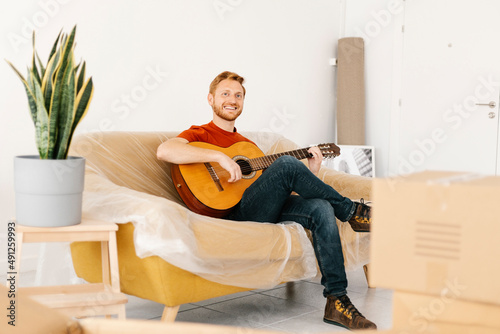 Happy man with guitar sitting on sofa at home