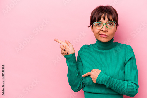 Young hispanic woman isolated on pink background shocked pointing with index fingers to a copy space.