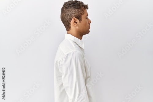 Young handsome hispanic man standing over isolated background looking to side, relax profile pose with natural face with confident smile.