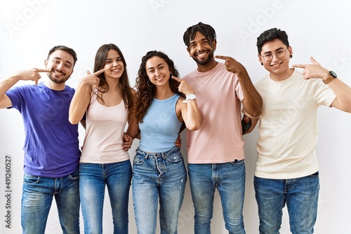 Group of young people standing together over isolated background smiling cheerful showing and pointing with fingers teeth and mouth. dental health concept.