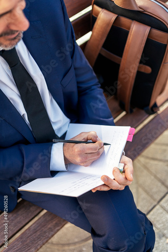 Unrecognizable businessman taking notes in notepad in city