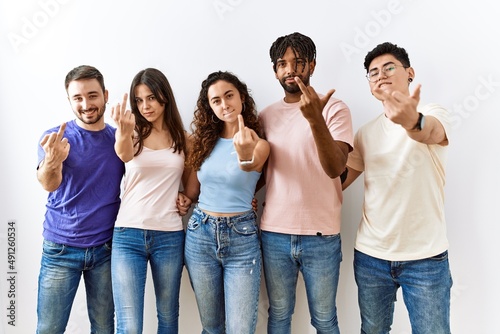Group of young people standing together over isolated background showing middle finger, impolite and rude fuck off expression
