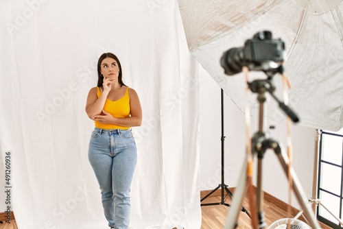 Young beautiful hispanic woman posing as model at photography studio with hand on chin thinking about question  pensive expression. smiling with thoughtful face. doubt concept.