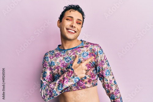 Handsome man wearing make up wearing fashion clothes cheerful with a smile of face pointing with hand and finger up to the side with happy and natural expression on face