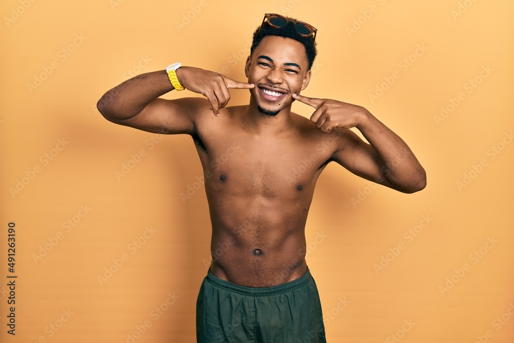 Young african american man wearing swimwear and swimmer glasses smiling cheerful showing and pointing with fingers teeth and mouth. dental health concept.