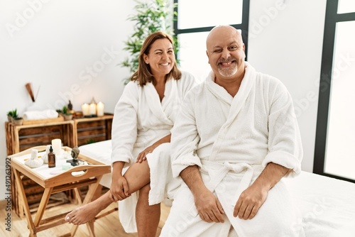 Middle age hispanic couple wearing bathrobe at wellness spa winking looking at the camera with sexy expression, cheerful and happy face.