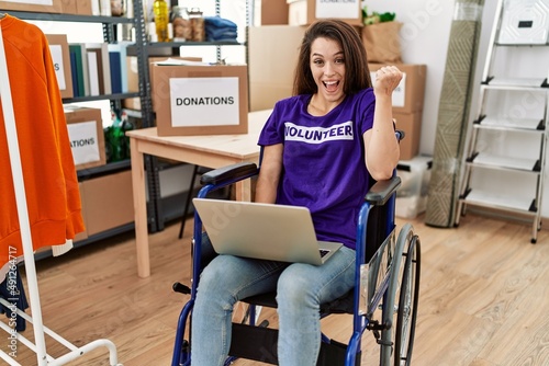 Young brunette woman as volunteer on donations stand sitting on wheelchair screaming proud, celebrating victory and success very excited with raised arms © Krakenimages.com