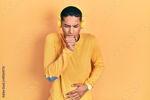 Young african american guy listening to music using headphones feeling unwell and coughing as symptom for cold or bronchitis. health care concept.