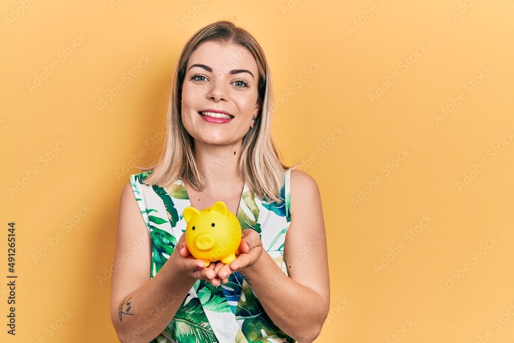 Beautiful caucasian woman holding piggy bank smiling with a happy and cool smile on face. showing teeth.