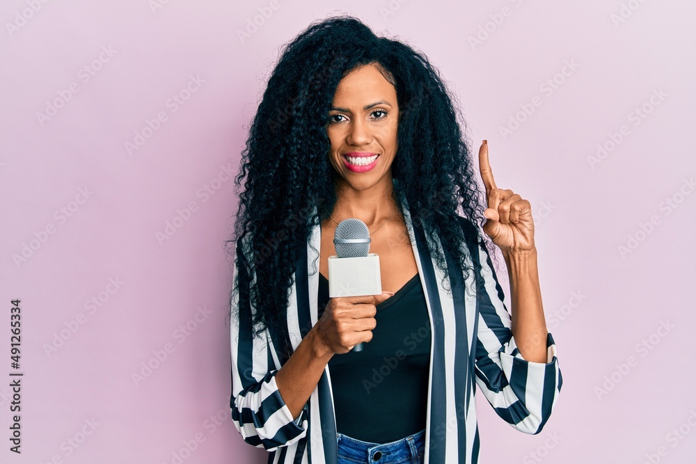 Middle age african american woman holding reporter microphone smiling with an idea or question pointing finger with happy face, number one Middle age african american woman holding reporter microphone smiling with an idea or question pointing finger with happy face, number one