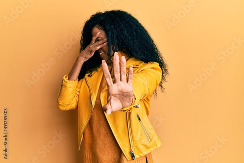 Middle age african american woman wearing wool winter sweater and leather jacket covering eyes with hands and doing stop gesture with sad and fear expression. embarrassed and negative concept. photo