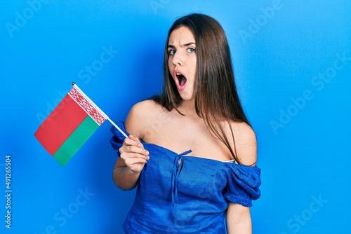 Young brunette teenager holding belarus flag scared and amazed with open mouth for surprise  disbelief face