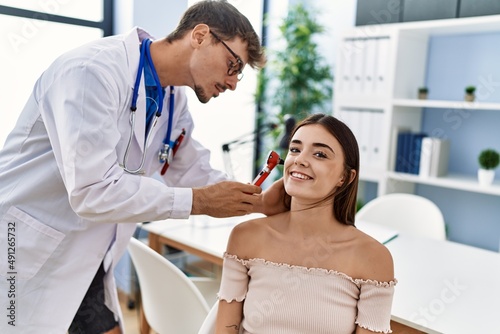 Man and woman wearing doctor uniform auscultating ear using otoscope at clinic