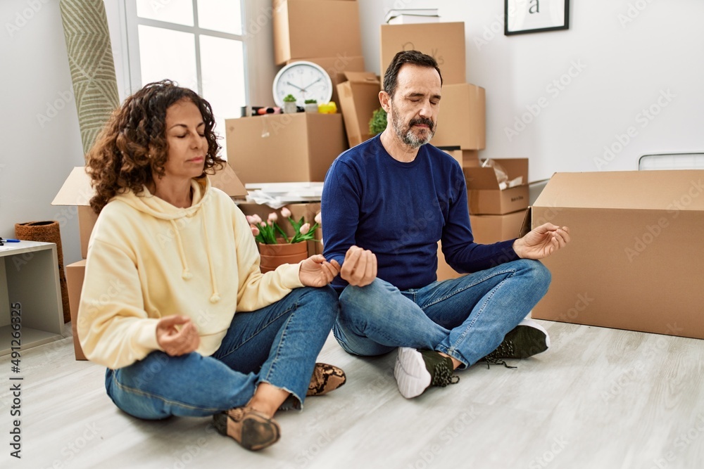 Middle age hispanic couple concentrated sitting on the floor doing yoga pose new home.