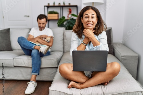 Hispanic middle age couple at home, woman using laptop shouting and suffocate because painful strangle. health problem. asphyxiate and suicide concept.
