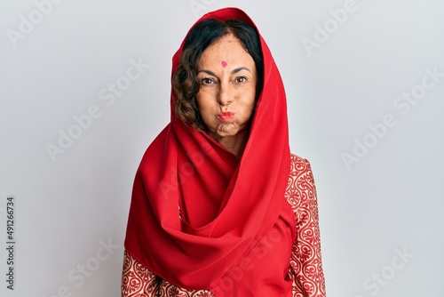 Middle age hispanic woman wearing tradition sherwani saree clothes puffing cheeks with funny face. mouth inflated with air, crazy expression.