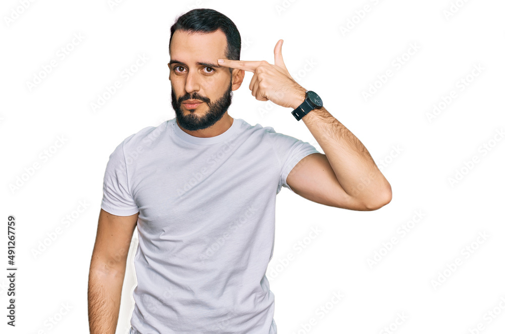 Young man with beard wearing casual white t shirt pointing unhappy to pimple on forehead, ugly infection of blackhead. acne and skin problem Young man with beard wearing casual white t shirt pointing unhappy to pimple on forehead, ugly infection of blackhead. acne and skin problem