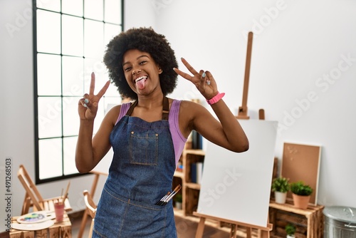 Photography Young african american woman with afro hair at art studio smiling with tongue out showing fingers of both hands doing victory sign