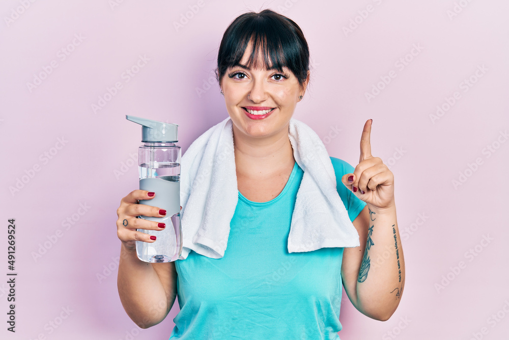 Young hispanic woman wearing sportswear holding water bottle smiling with an idea or question pointing finger with happy face, number one Young hispanic woman wearing sportswear holding water bottle smiling with an idea or question pointing finger with happy face, number one