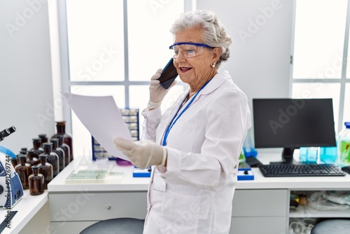 Senior grey-haired woman wearing scientist uniform talking on the smartphone at laboratory