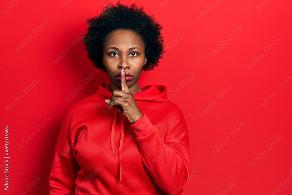 Young african american woman wearing casual sweatshirt asking to be quiet with finger on lips. silence and secret concept. - obrazy, fototapety, plakaty 