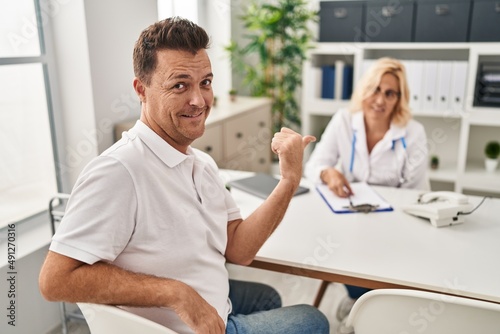 Hispanic man at the doctor smiling happy pointing with hand and finger