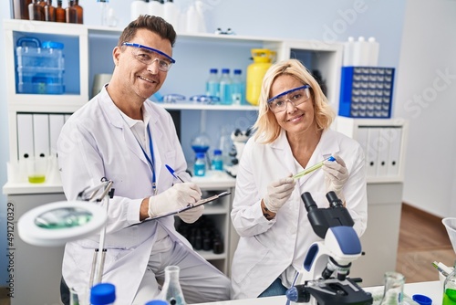 Middle age man and woman scientist partners working using microscope and test tube at laboratory