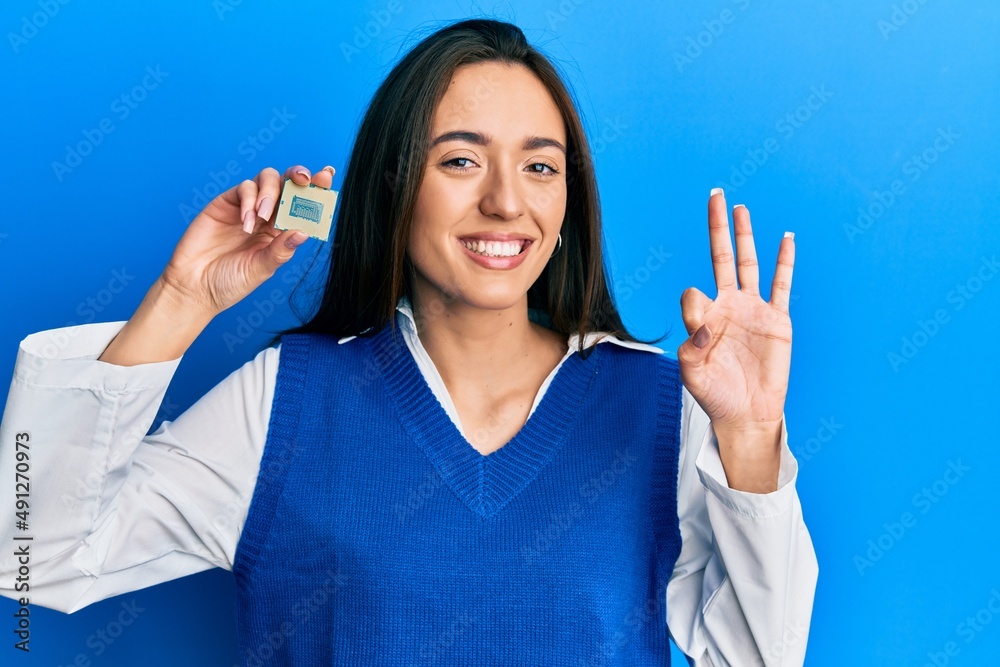 Young hispanic girl holding cpu computer processor doing ok sign with fingers, smiling friendly gesturing excellent symbol Young hispanic girl holding cpu computer processor doing ok sign with fingers, smiling friendly gesturing excellent symbol