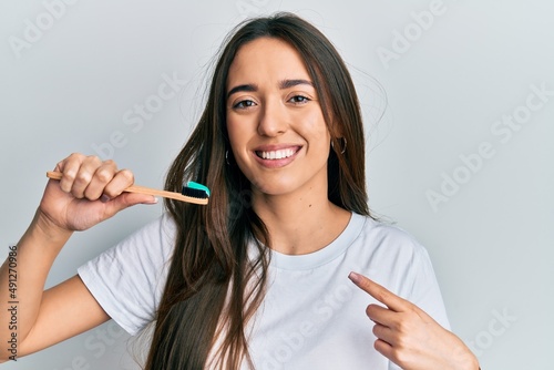Young hispanic girl holding toothbrush with toothpaste smiling happy pointing with hand and finger