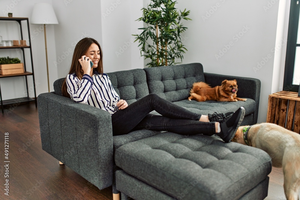 Young hispanic woman talking on the smartphone sitting on sofa with dogs at home Young hispanic woman talking on the smartphone sitting on sofa with dogs at home