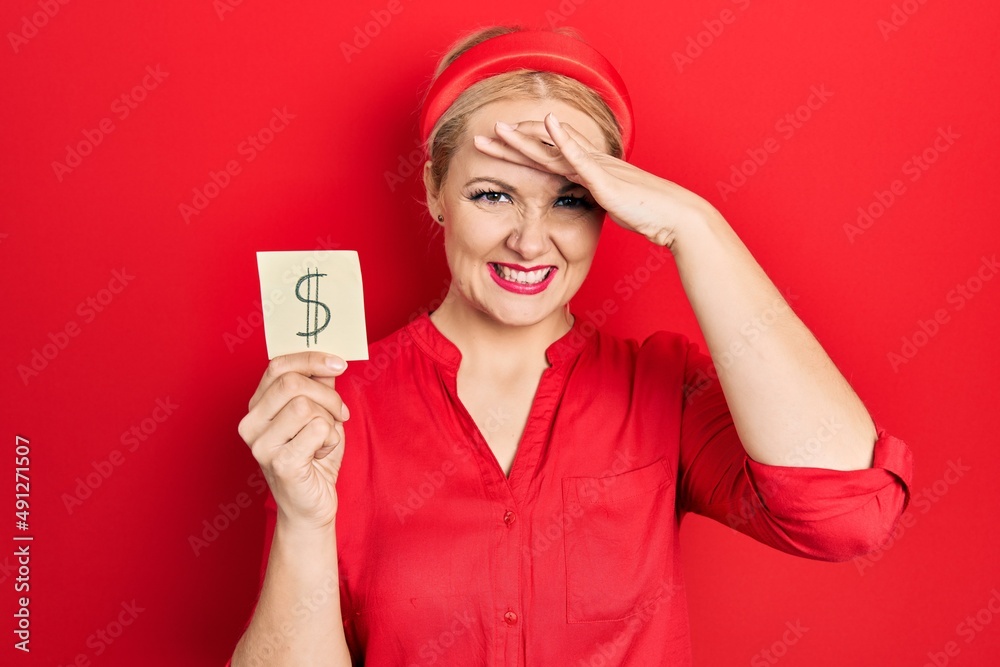 Young blonde woman holding dollar symbol reminder paper stressed and frustrated with hand on head, surprised and angry face Young blonde woman holding dollar symbol reminder paper stressed and frustrated with hand on head, surprised and angry face