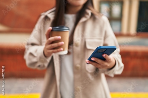 Young hispanic woman using smartphone drinking coffee at street