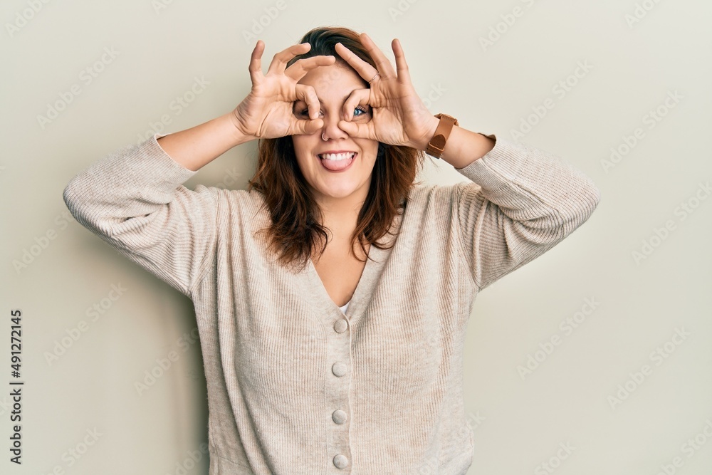 Young caucasian woman wearing casual clothes doing ok gesture like binoculars sticking tongue out, eyes looking through fingers. crazy expression. Young caucasian woman wearing casual clothes doing ok gesture like binoculars sticking tongue out, eyes looking through fingers. crazy expression.