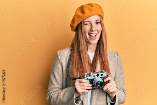 Young irish woman holding vintage camera winking looking at the camera with sexy expression, cheerful and happy face.