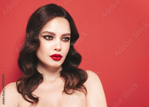Beauty portrait of young brunette woman with evening makeup and perfect clean skin. Sexy model with curly hair posing in studio. With red bright natural lips. Isolated on red background