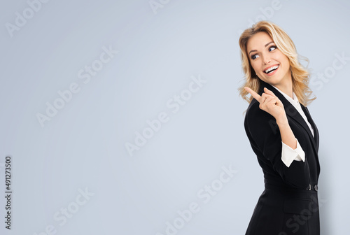 Portrait of happy smiling cheerful businesswoman, showing point away side with finger free copy space area for slogan or text, on grey background