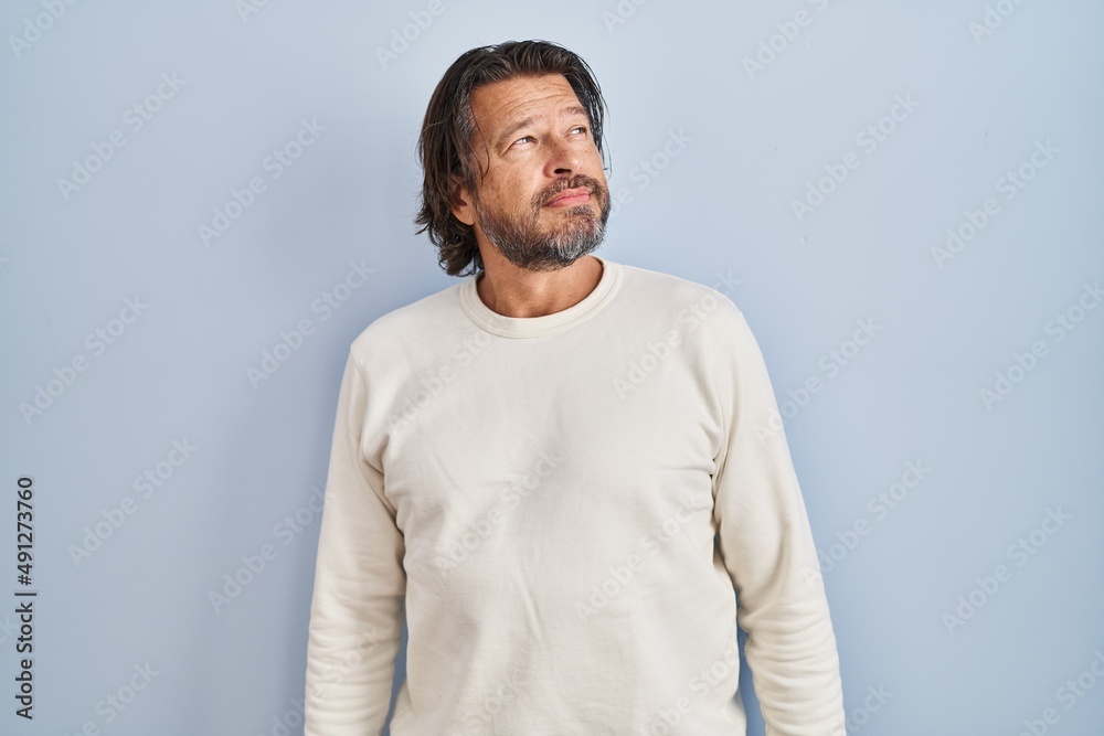 Handsome middle age man wearing casual sweater over blue background looking away to side with smile on face, natural expression. laughing confident.